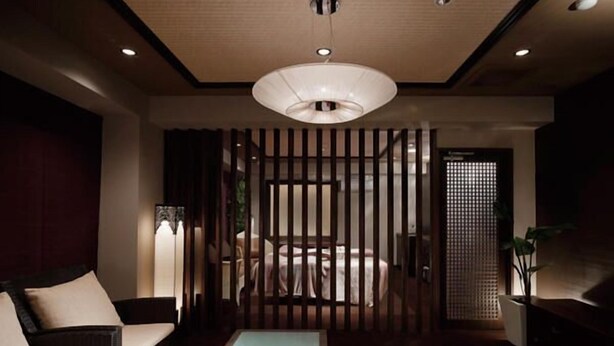 Un salon moderne comprenant un canapé, une table basse en verre agrémentée de fleurs, un coin repas avec une table et des chaises, et un élément de séparation décoratif composé de lattes verticales.