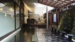 Un espace intérieur moderne doté d’un sol en pierre, d’un coin salon avec des chaises et des tables, et d’une pergola en bois surmontée d’un auvent blanc.