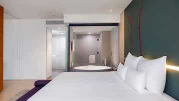 A modern hotel room with a large bed, a bathroom with a round bathtub, and a visible shower area.