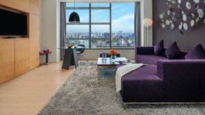 Una sala de estar moderna con vista a la ciudad, una mesa de centro de vidrio, un sofá púrpura y un televisor de pantalla plana montado en la pared.