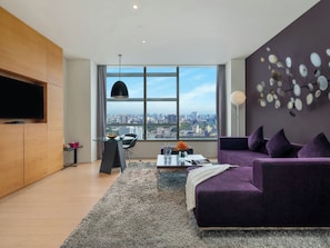 A modern living room with a city view, a glass coffee table, a purple sofa, and a flat-screen TV mounted on the wall.