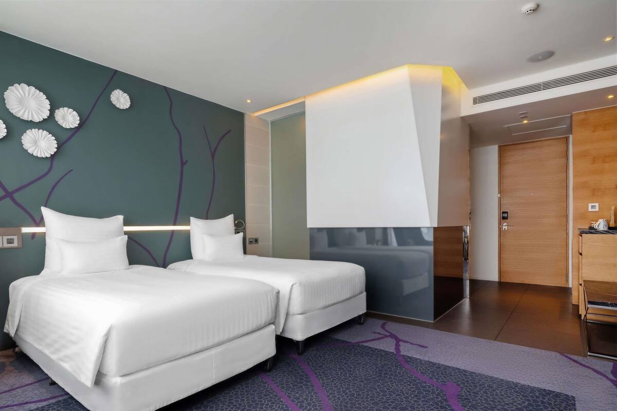 Ein Hotelzimmer mit zwei Betten, modernem Design, einem großen Spiegel und einer Holztür.