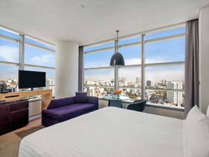 Habitación de hotel con una cama grande, un escritorio con televisor, un sofá y vistas a la ciudad.