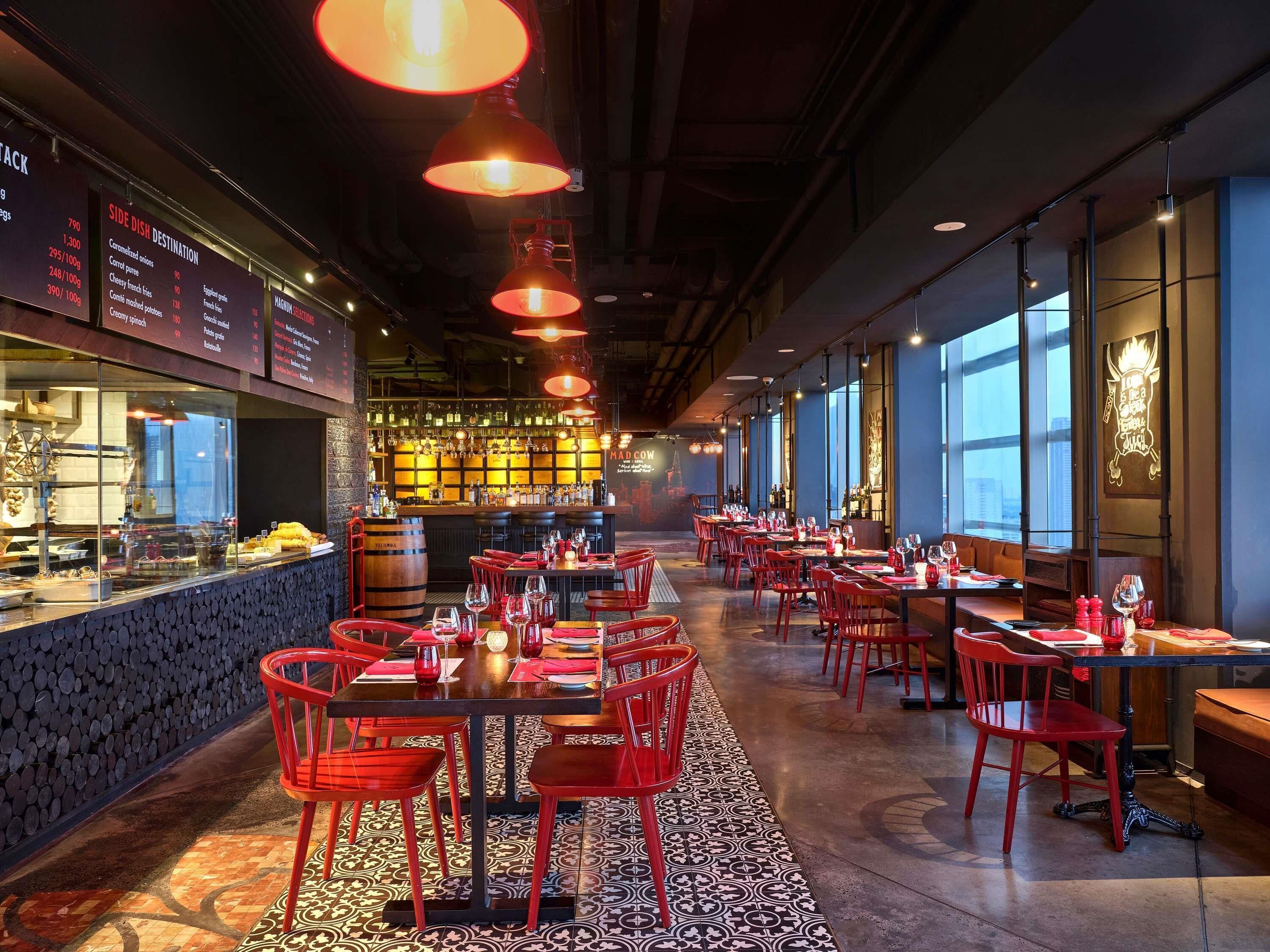 Ein Restaurantinneres mit Barbereich, roten Stühlen und gedeckten Tischen.