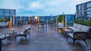 Un bar en la azotea con mesas, sillas y una barra, con vistas a la ciudad.