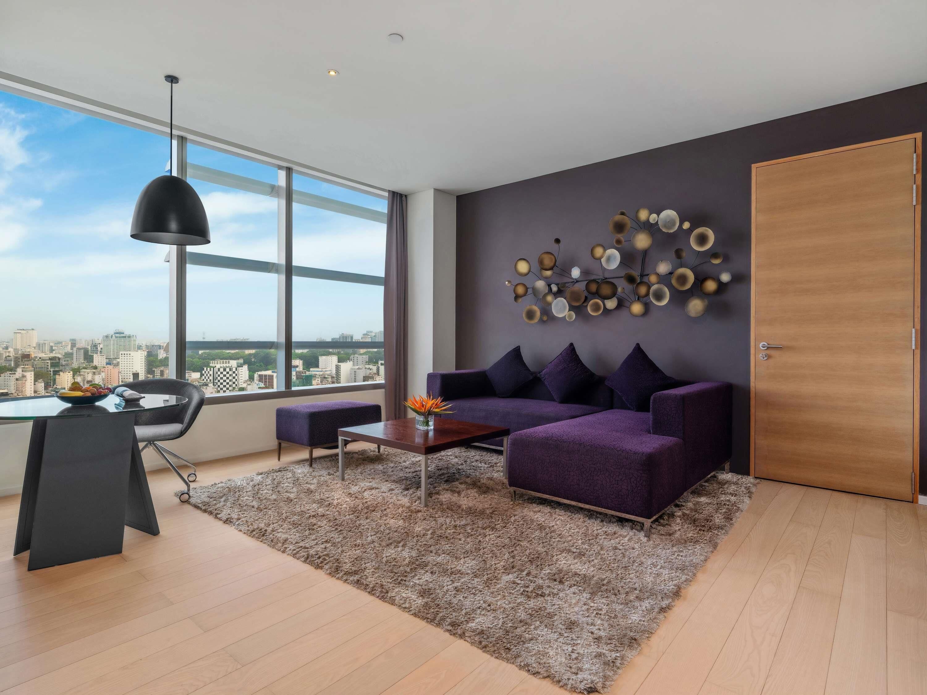 Una sala de estar moderna con un amplio ventanal, un sofá morado, una mesa de centro y vistas a la ciudad.
