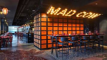 Interior de restaurante con barra, varias mesas y una pared distintiva con letras iluminadas.