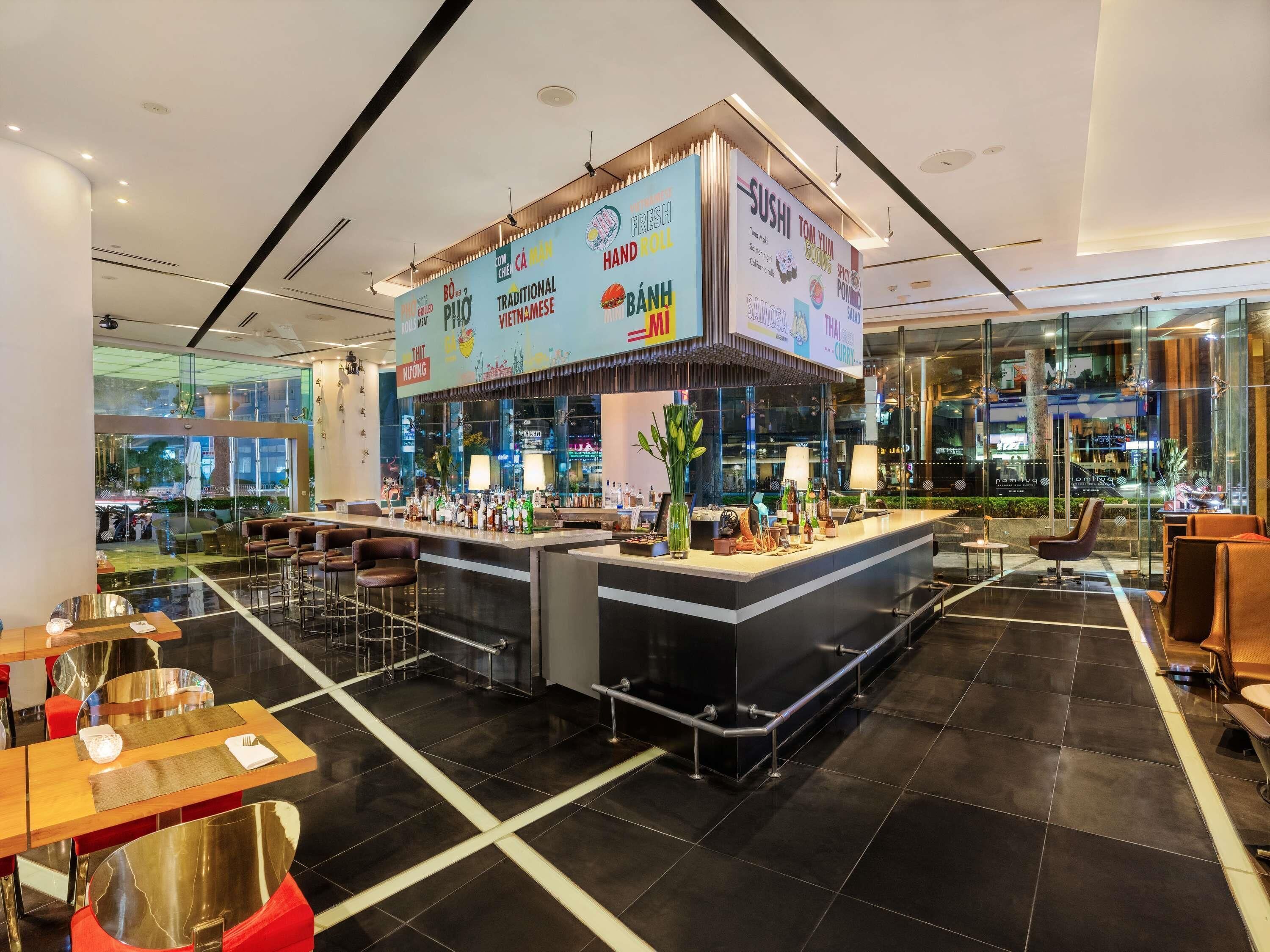 Un espace bar moderne doté d’un comptoir central, de différents types de sièges et d’un mur en verre.