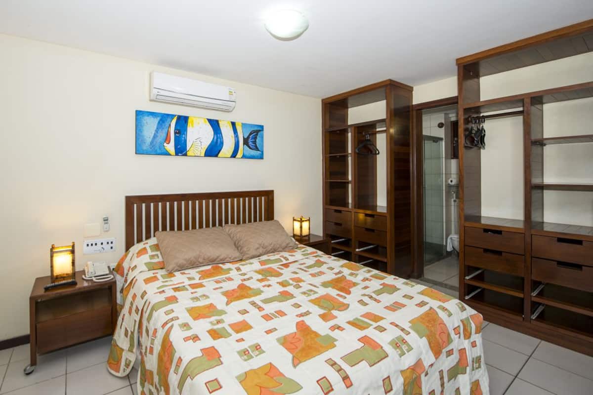 A bedroom with a bed, nightstands, a wardrobe, and an air conditioning unit.