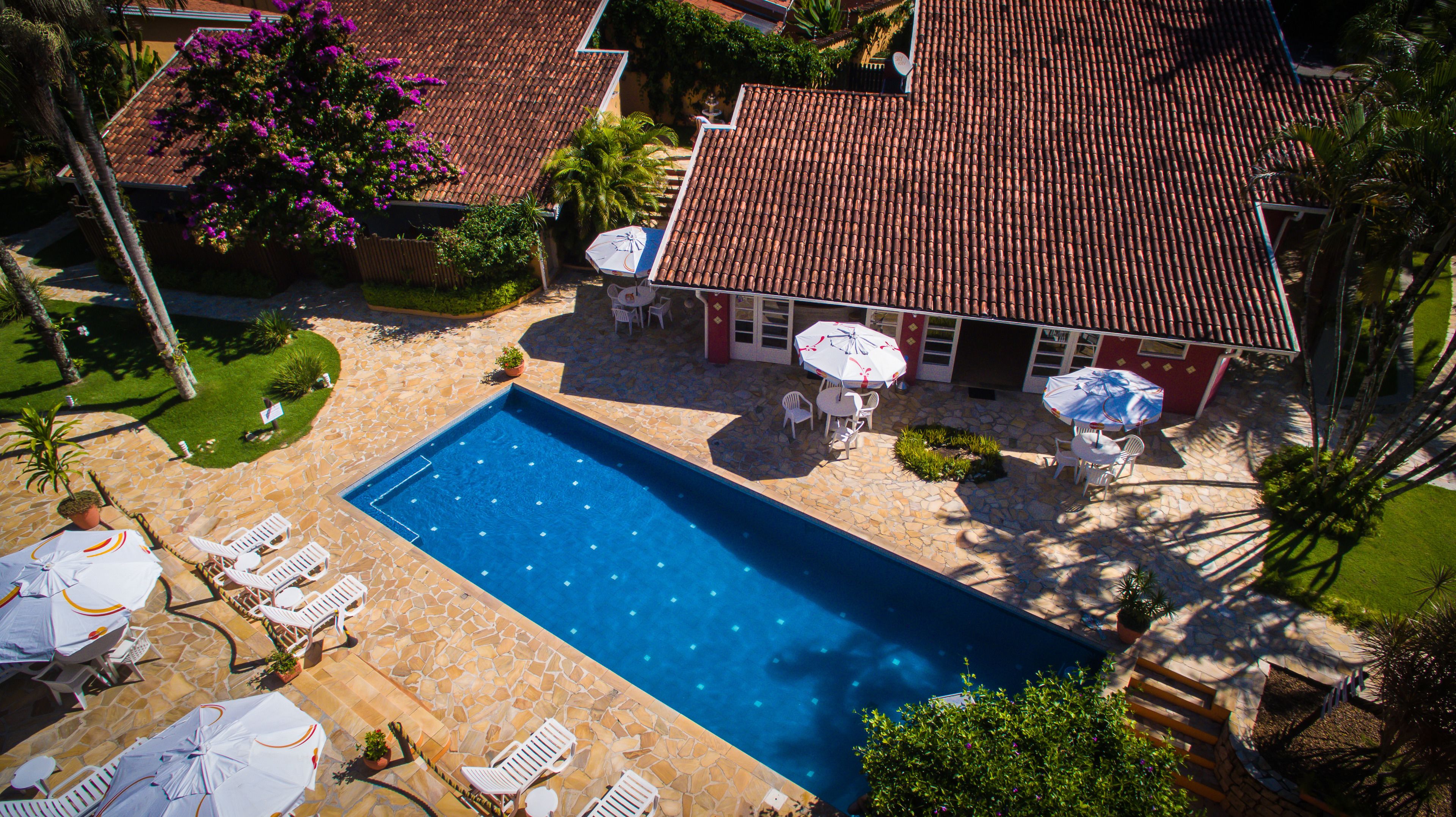 An aerial view of a property with a swimming pool, stone patio, and outdoor seating area with umbrellas.