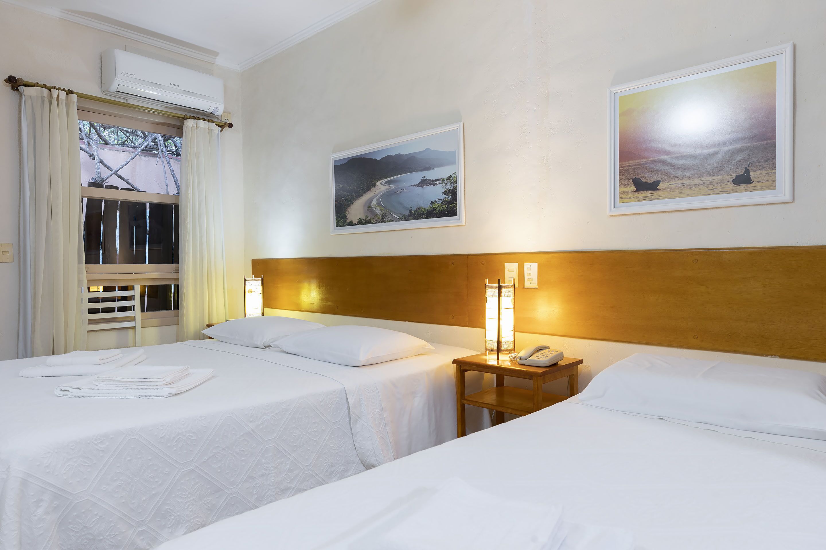 A hotel room with two beds, a wooden headboard, a nightstand with a lamp, and a framed landscape painting.