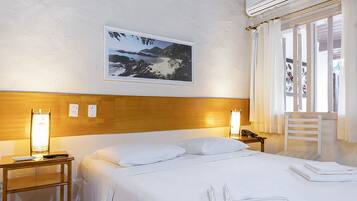 A hotel room with two beds, a wooden headboard, a ceiling fan, a window with curtains, and a painting on the wall.