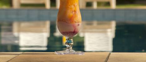 A cocktail with a straw, placed on a table near a poolside with white lounge chairs in the background.