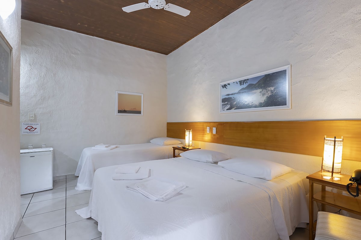 Une chambre d’hôtel avec deux lits, une tête de lit en bois, une table de chevet avec une lampe et une petite table avec un téléphone.