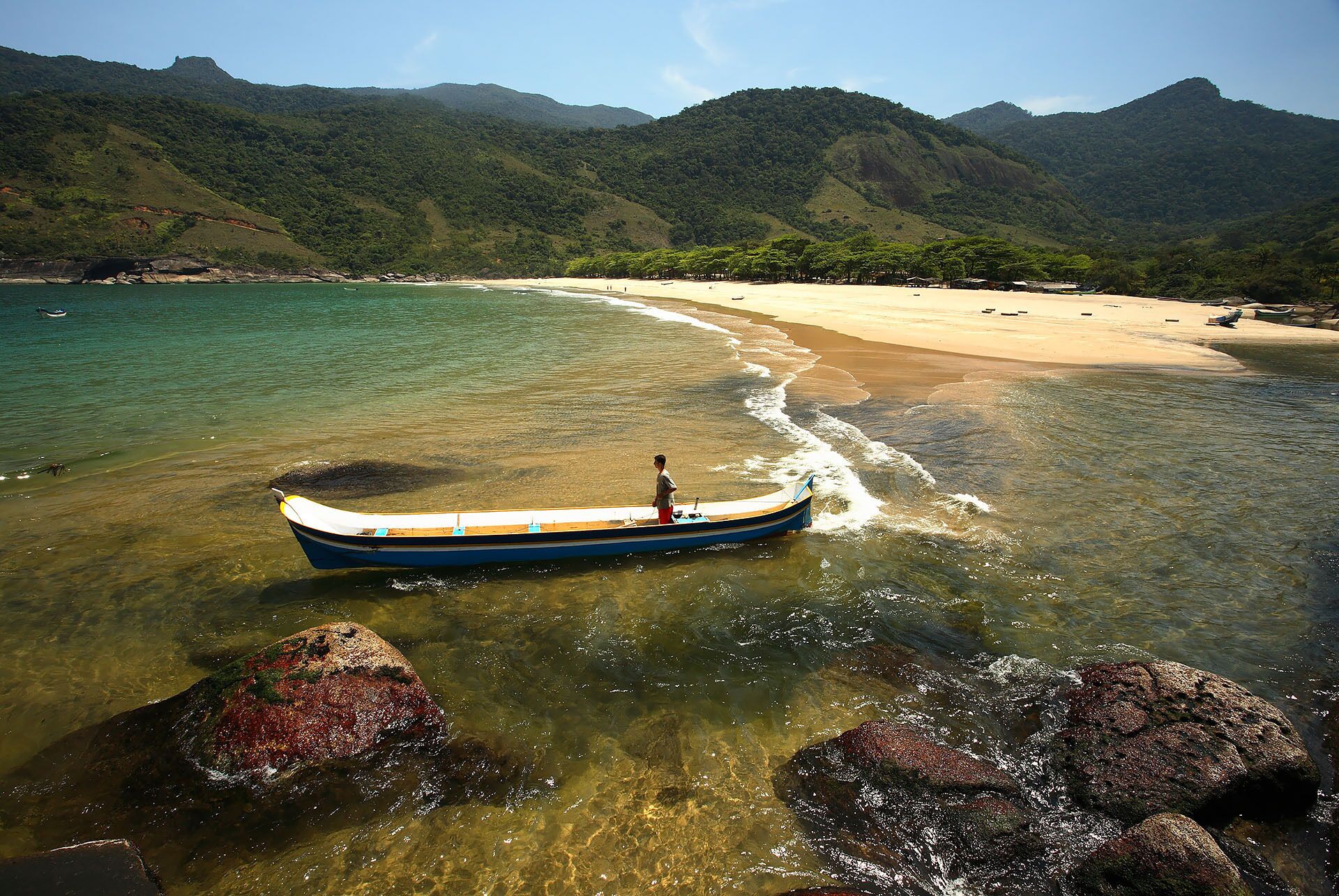 Un bateau sur une plage de sable fin, avec des affleurements rocheux et des montagnes en arrière-plan.
