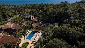 Vue aérienne d’un complexe hôtelier doté d’une piscine, entouré d’une végétation luxuriante et avec des montagnes en arrière-plan.