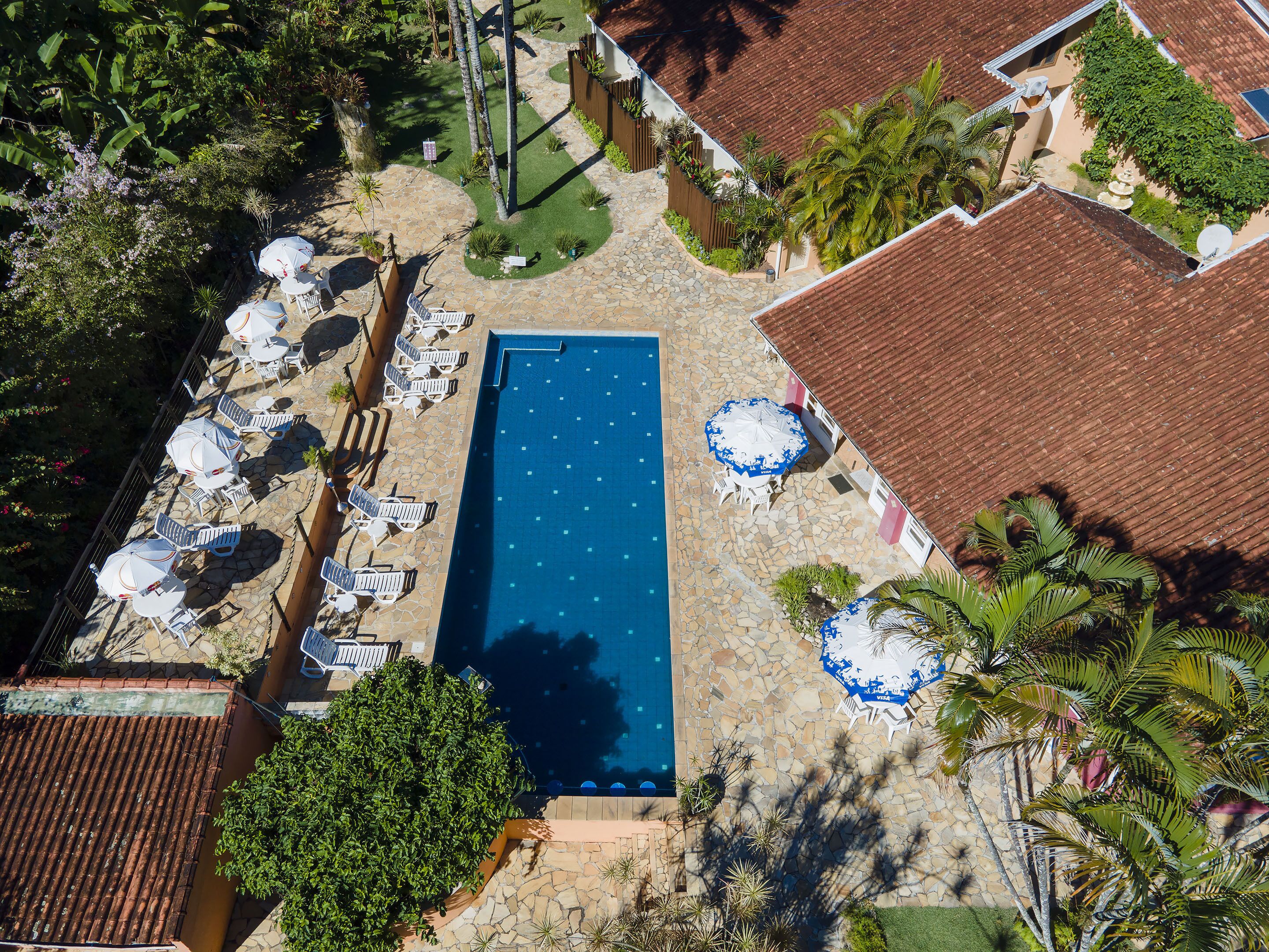 An aerial view of a resort with a swimming pool, sun loungers, and tropical landscaping.