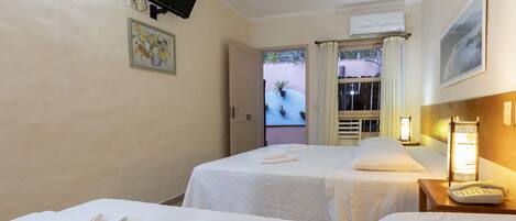 A hotel room with two beds, a flat-screen TV mounted on the wall, an air conditioning unit, a painting, and a view of the outside.