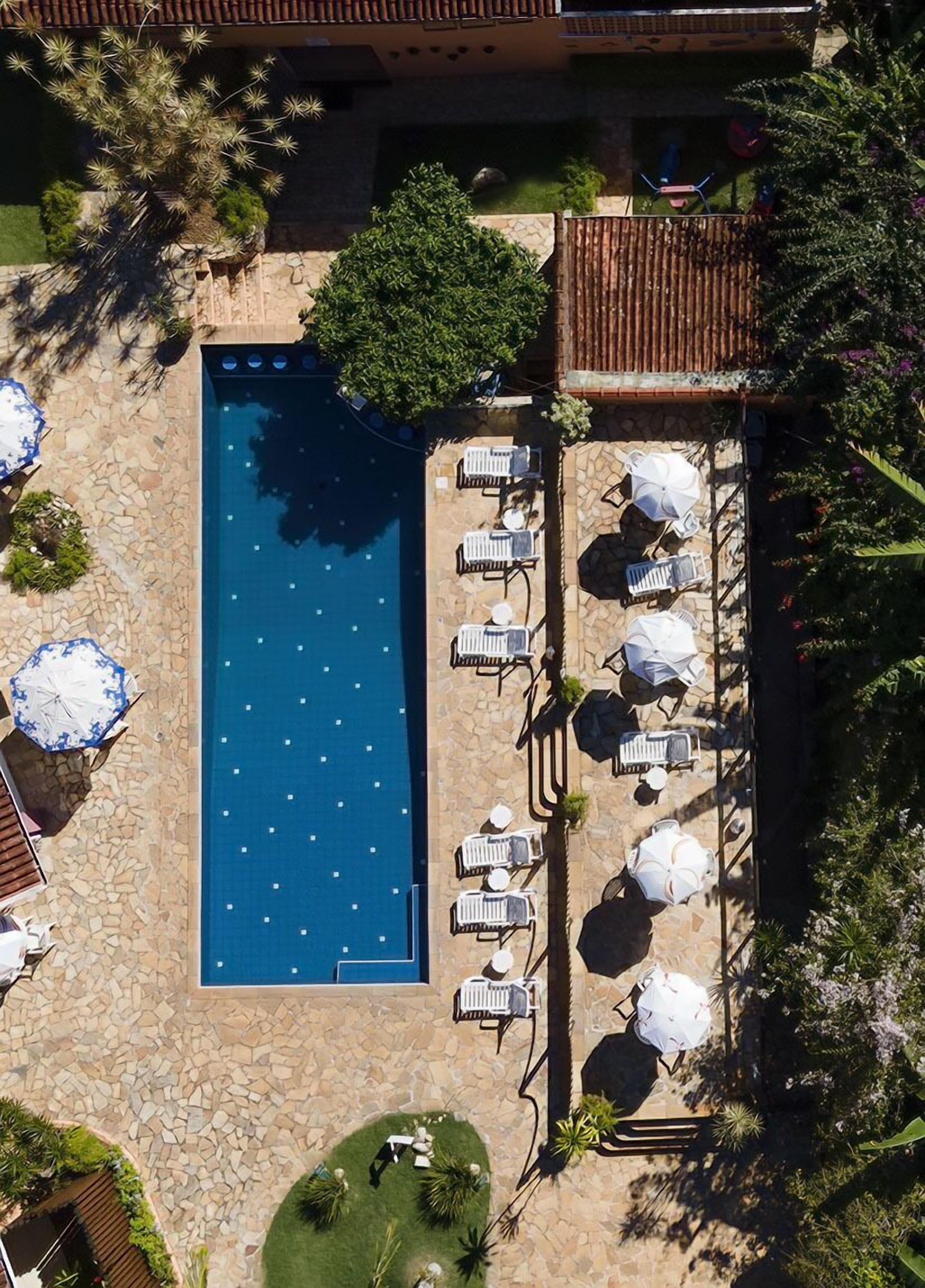 Vista aérea de una piscina rectangular rodeada de baldosas de piedra, con sillones y sombrillas dispuestas a lo largo de la piscina.