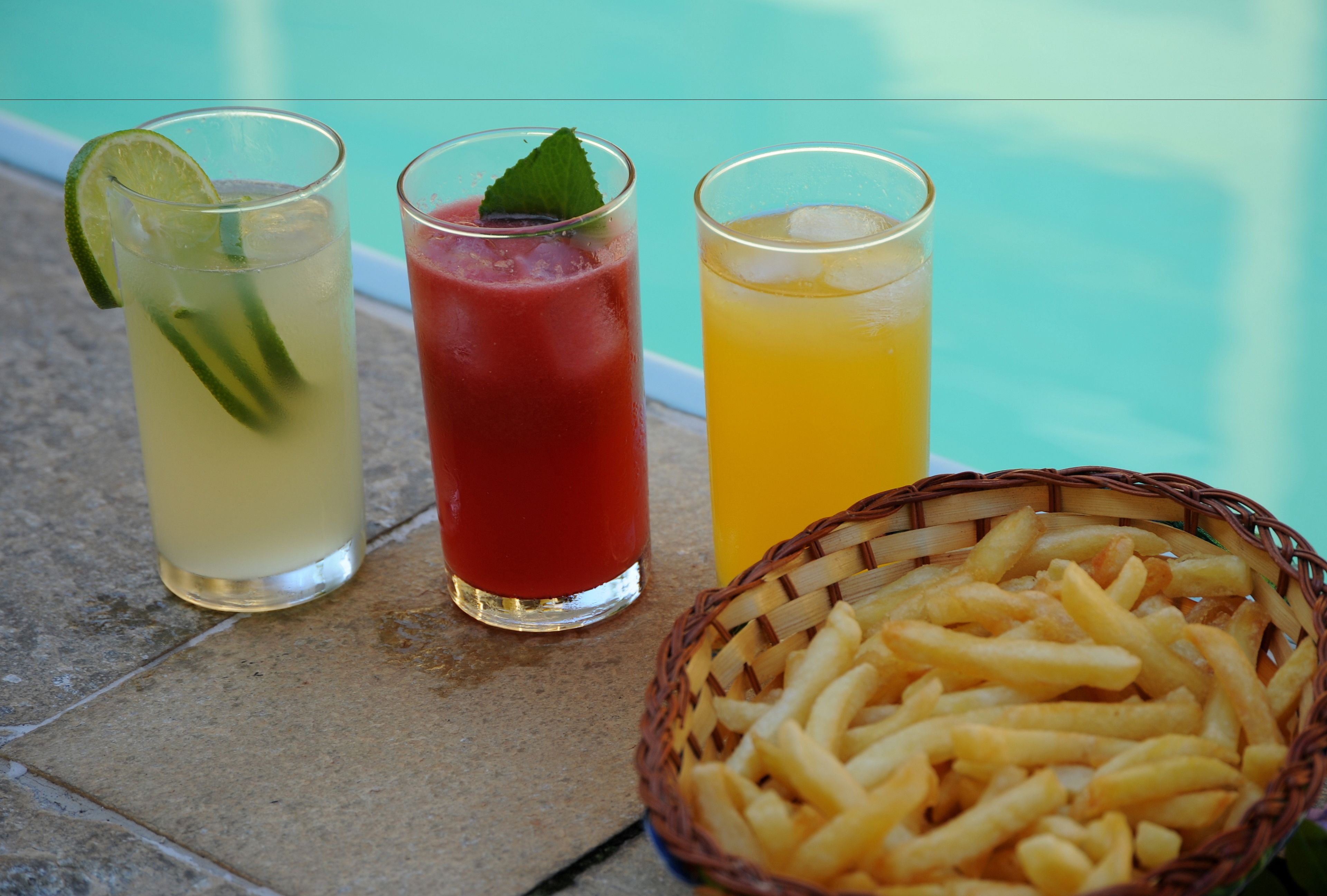 Three glasses of beverages with a basket of fries.
