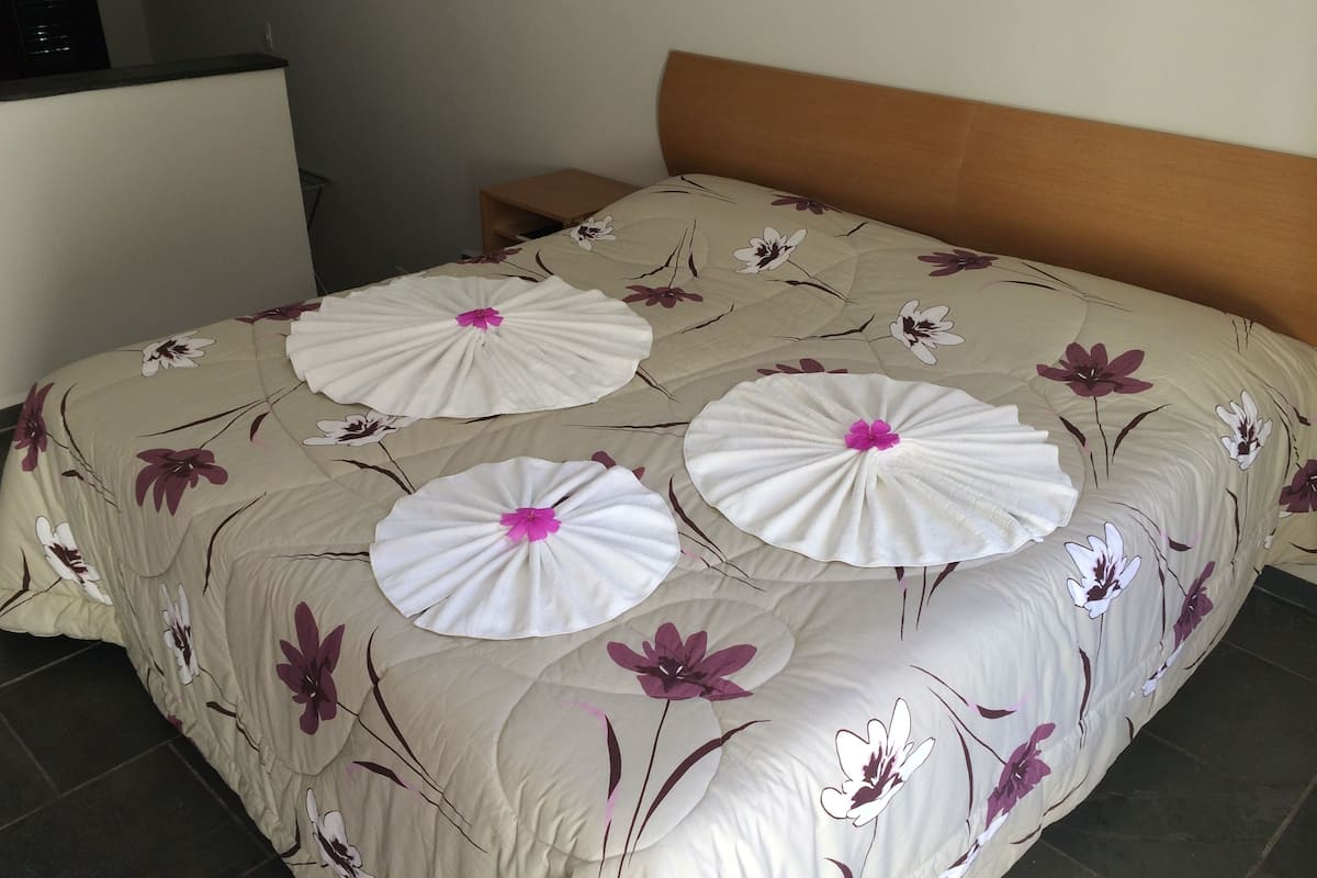A bed with a floral bedspread and three white pillows with pink flowers.