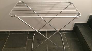 A metal drying rack with a crossbar design, placed on a tiled floor against a plain wall.