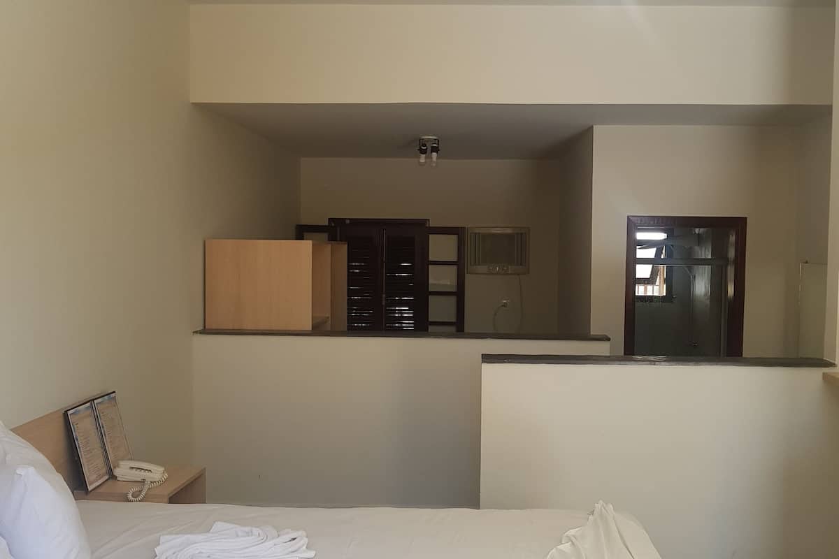 A hotel room with a bed, a desk with a telephone, and a kitchenette area.