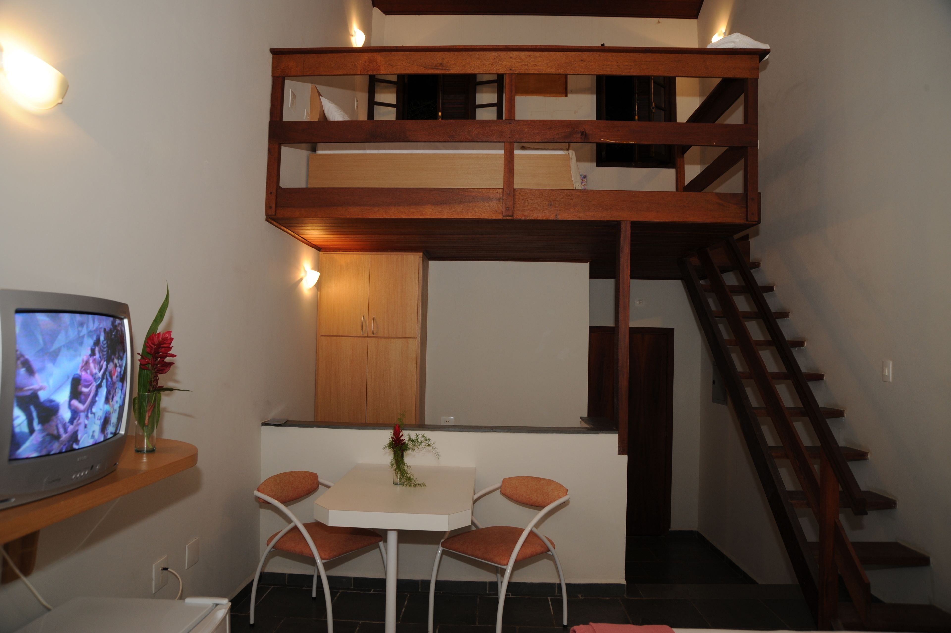 Una habitación pequeña con literas, una mesita con dos sillas, televisión y una escalera de madera.