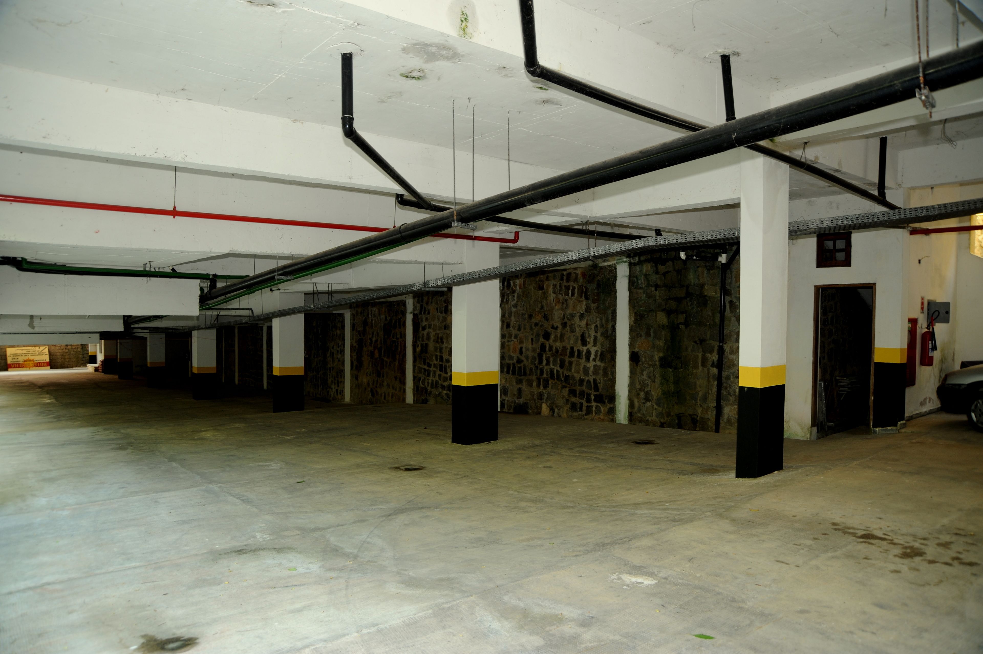 An empty parking garage with concrete floors, white pillars with yellow bands, and exposed pipes on the ceiling.