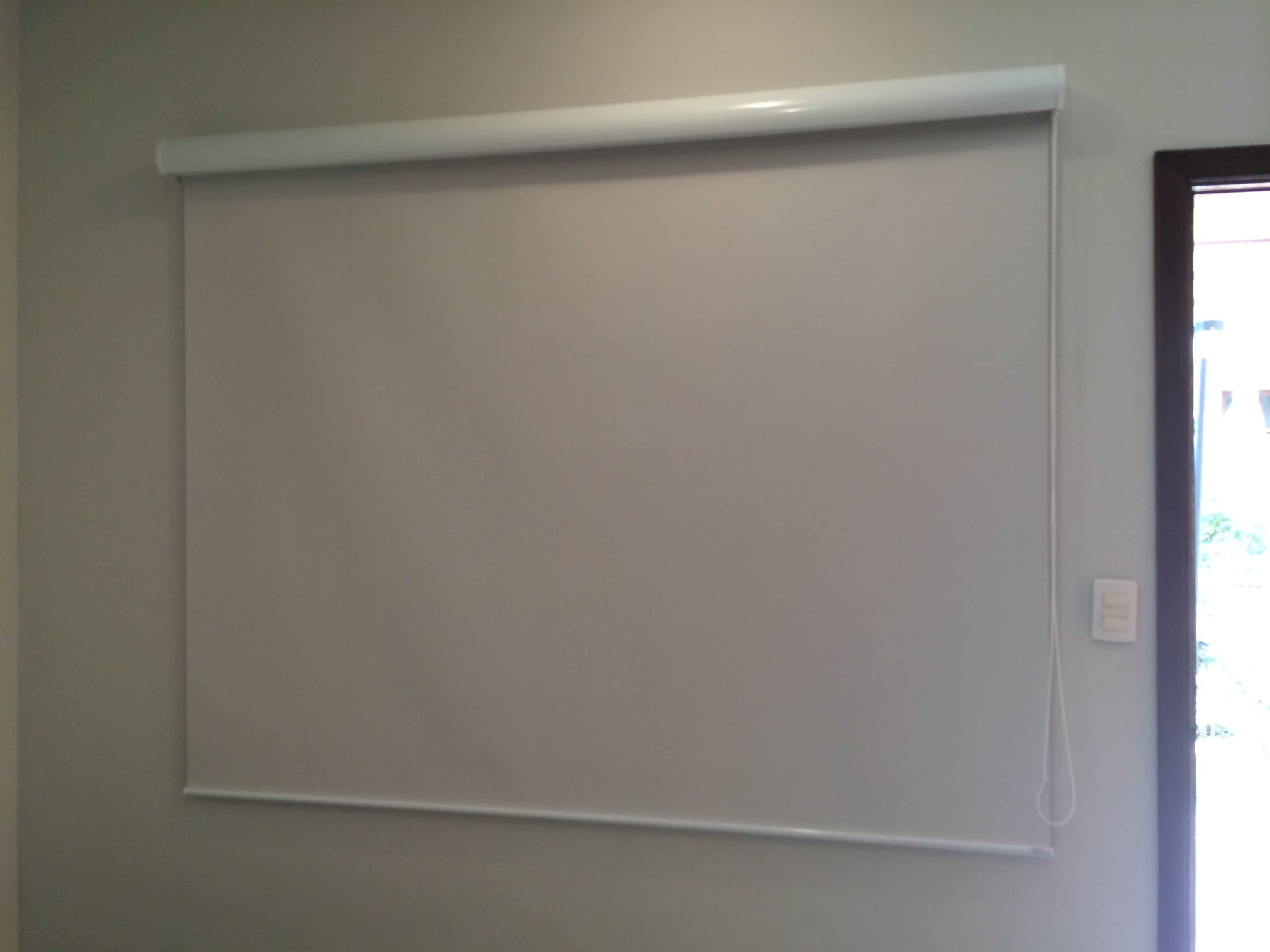Una pared blanca con una pantalla proyectora blanca sujeta al techo.
