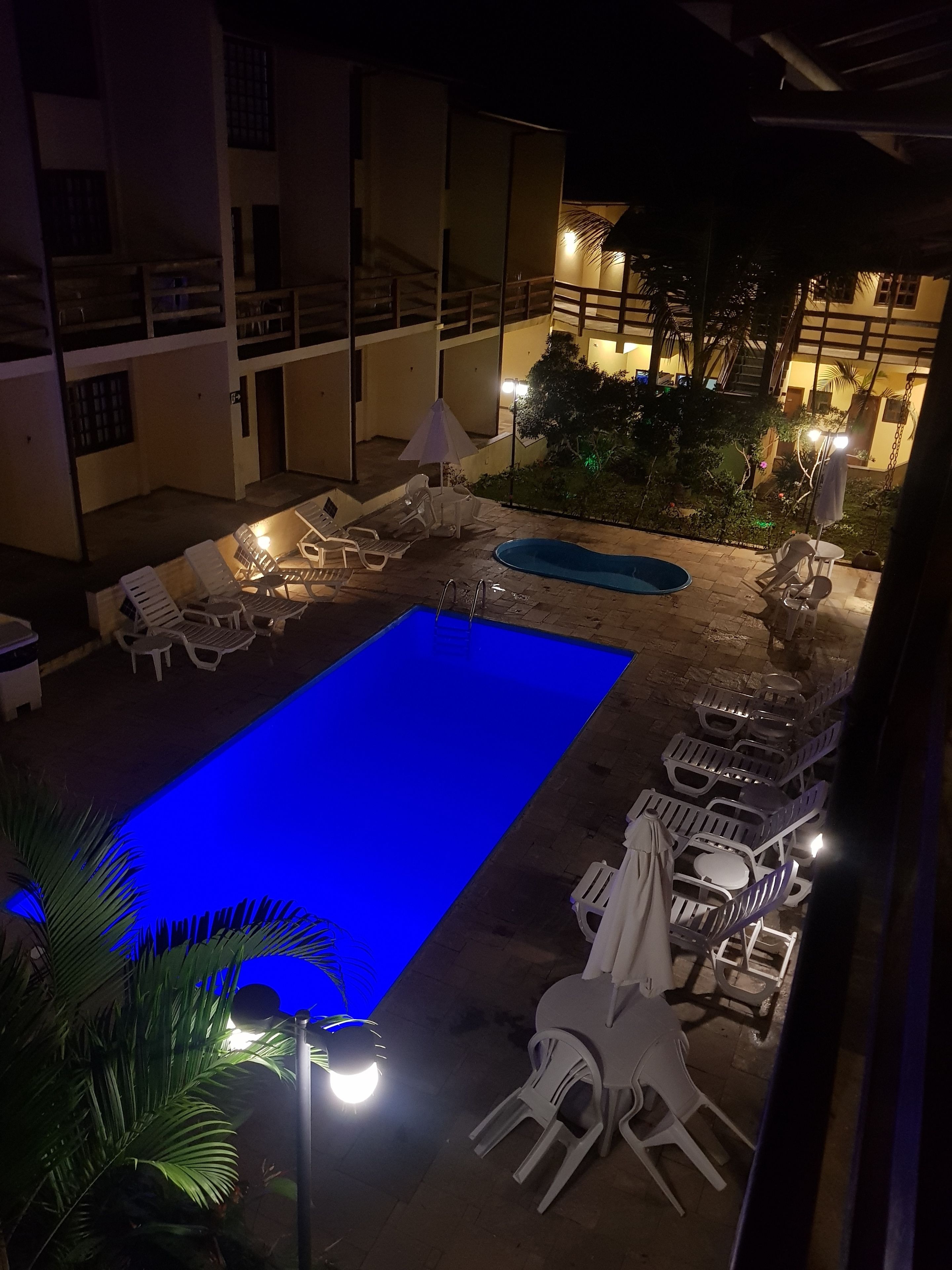 A nighttime view of a pool area with a blue-lit pool, white lounge chairs, and umbrellas.
