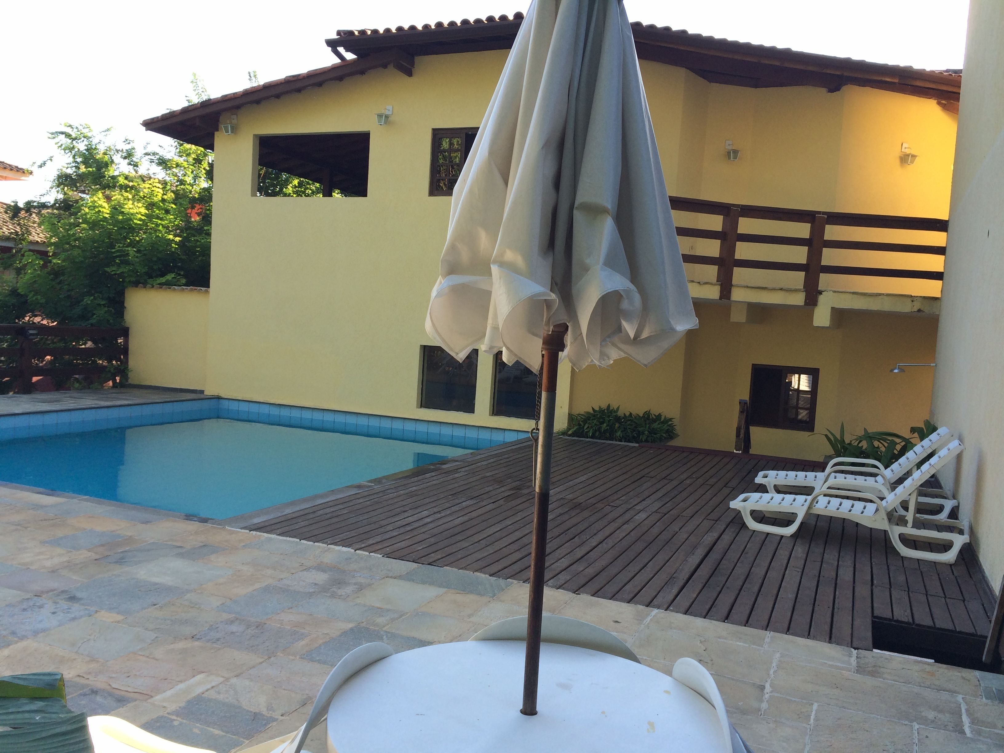 Zona junto a la piscina con una sombrilla blanca, sillas de descanso y una terraza de madera.