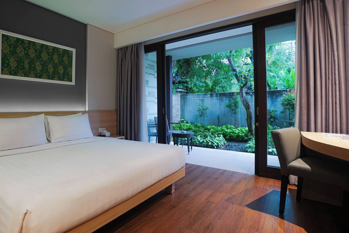 Une chambre d’hôtel avec un grand lit, un bureau et une vue sur un jardin, accessible par une porte coulissante.