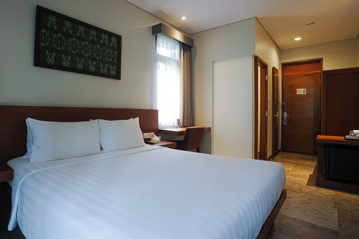 Une chambre d’hôtel avec un grand lit, une table de chevet avec un téléphone, un bureau avec une chaise et une porte donnant sur une salle de bain.