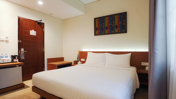 Habitación de hotel con una cama grande, cabecera de madera, mesita de noche, cafetera, una obra de arte enmarcada en la pared y una puerta con un letrero.