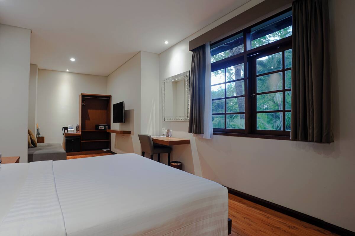 Une chambre d’hôtel avec un grand lit, un bureau, une chaise, une armoire, une télévision et une fenêtre donnant sur un paysage verdoyant.