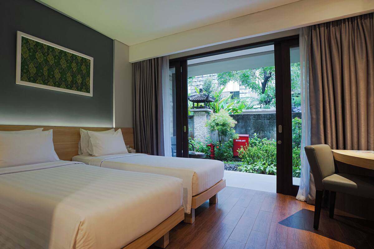 Une chambre d’hôtel avec deux lits, un bureau et une vue sur un jardin.