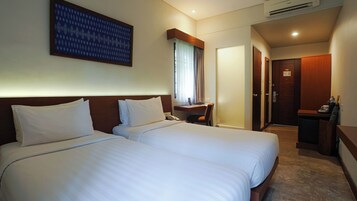 A hotel room with two beds, a desk, a chair, a telephone, and a door.