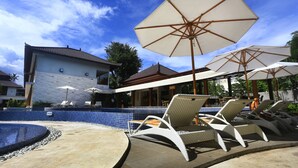 A pool area with lounge chairs and umbrellas, a tiled pool, and a building with a tiled exterior. - Grand Whiz Hotel Nusa Dua (Nusa Dua)