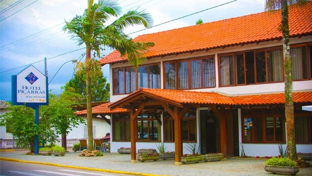 A hotel with a red-tiled roof, a covered patio area, and a signboard. - Hotel Piçarras (Picarras)