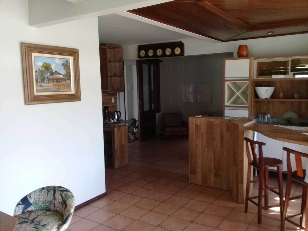 Uma cozinha com armários de madeira, uma área de jantar com banquetas e um piso ladrilhado.