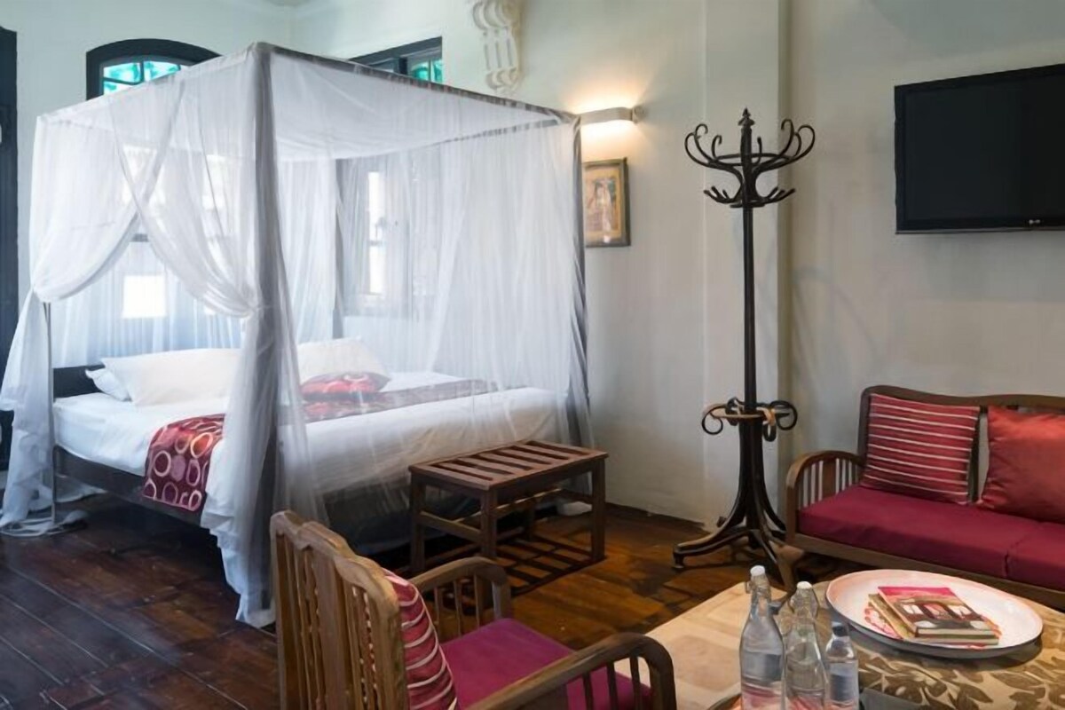 A room with a four-poster bed, a sofa, a table with a tray, and a television on the wall.