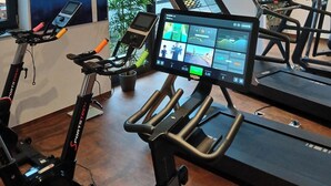 Een moderne sportschool met hometrainers, loopbanden en een digitaal scherm.