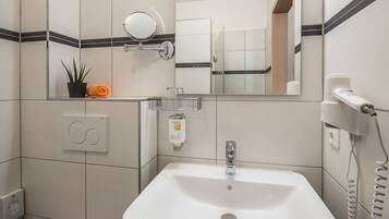 Un baño con lavamanos blanco, un espejo, toallero, planta en maceta y secador de pelo.