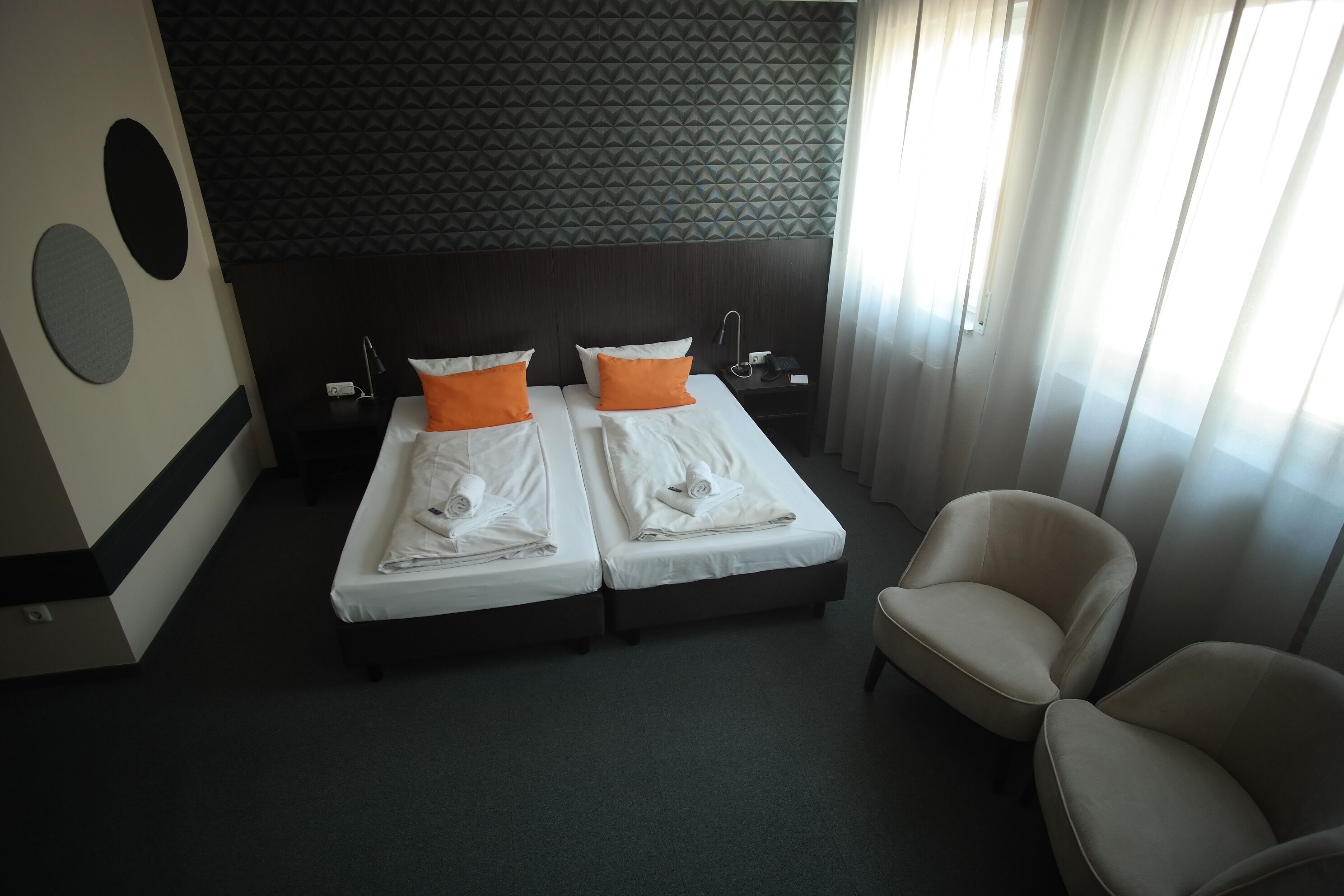 Une chambre d’hôtel avec deux lits, une chaise, une table de chevet et un mur orné d’un motif géométrique.