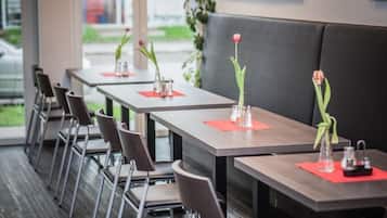A restaurant with multiple tables and chairs, each with a red placemat and a small vase with a flower.