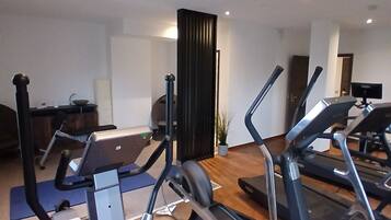Un gimnasio con diferentes máquinas de ejercicio, un escritorio y una planta en maceta.