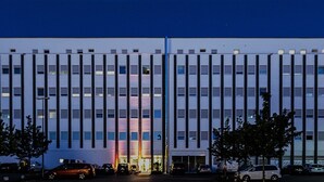 Een modern gebouw met een symmetrische gevel, meerdere ramen en een parkeerplaats met auto's.