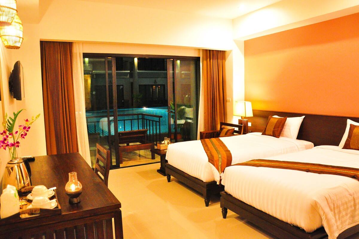 A hotel room with two beds, a dining table, a coffee maker, and a view of a pool through a glass door.