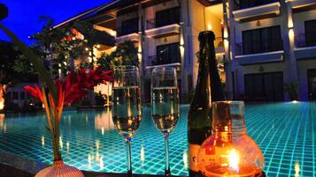 A poolside setting with two glasses of champagne, a bottle, and a candle on a table.